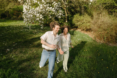 couple holding hands while running down a grassy hill with a magnolia tree in the background