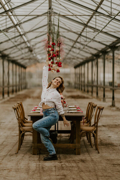 Laura souriante, bras levé, pose décontractée dans une verrière décorée pour un workshop pour photographe de mariage en Vendée.