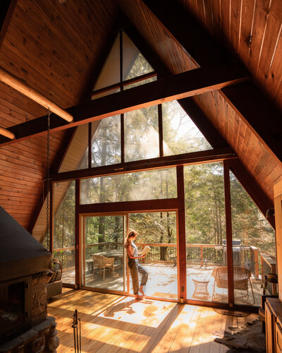Woman standing in front of windows inside a frame cabin