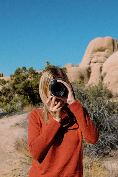 Nikki takes a photo with her camera, a desert landscape behind her.