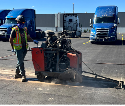 An operator in a safety vest and hard hat using a slab saw to cut concrete.