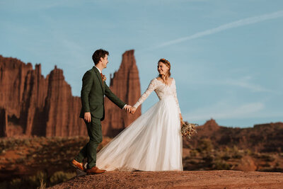 bride and groom holding hands in the desert with large red rock formations in the background