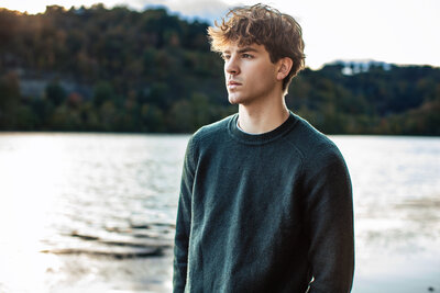 A portrait of a guy wearing a green sweater standing near the Ohio river in senior photos Pittsburgh Pennsylvania session.