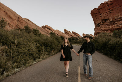man and woman holding hands during engagement photos at red rocks park in colorado.