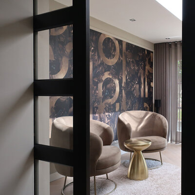 Twee velvet fauteuils in taupe kleur met gouden bijzettafel en donker luxe behang op de achtergrond