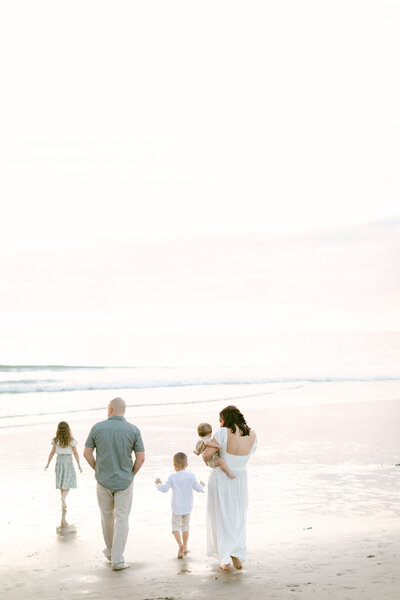 Family and 3 young children walk along the beach at sunset during family photography session