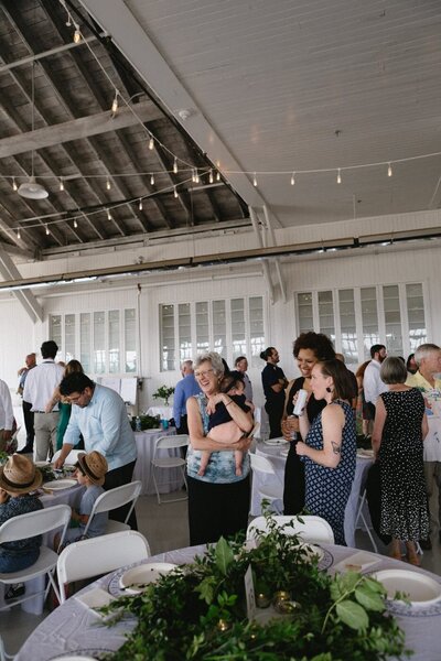 Guests at a reception in a high-ceilinged room talk with each other.