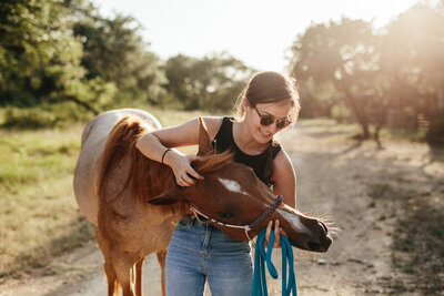 Girl with sunglasses scratches her horse's head lovingly