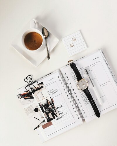 coffee, wrist watch, and calendar laid out on desk in flat lay. 