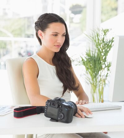 Image of a photographer sitting at a desk with a camera  looking at the screen of her computer