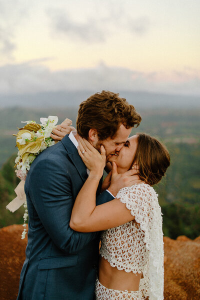 Bride and groom sharing an emotional kiss at sunset overlooking Waimea Canyon in Kauai during their intimate elopement.