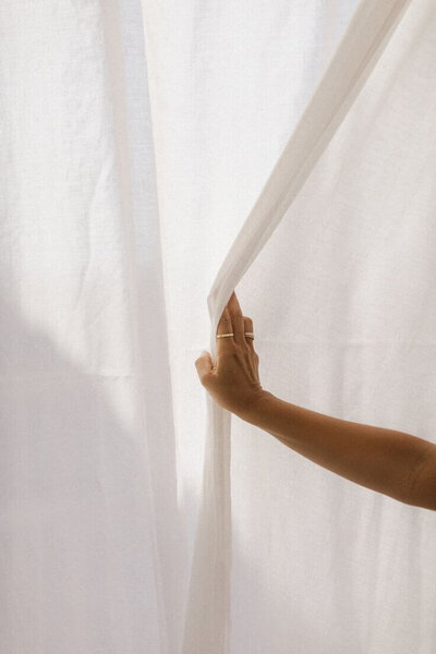 A hand parting white curtains, symbolizing unveiling new opportunities and stepping into clarity.