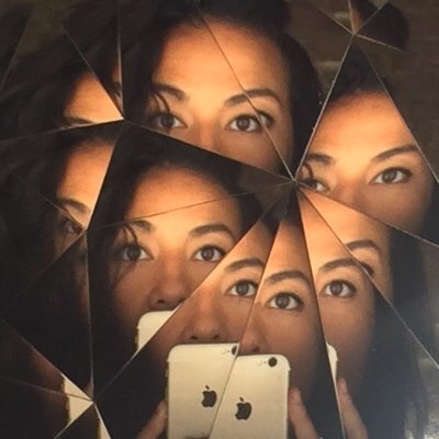 A woman taking a picture with her iphone of her reflection in a broken mirror, showing multiple fragmented pieces of her face