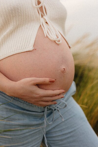 Closeup van zwangere buik tijdens zwangerschapsfotoshoot in de duinen