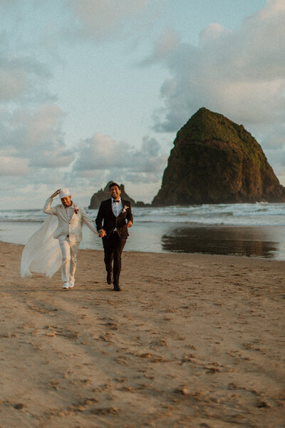 groom and groom holding hands running toward the camera on the beach