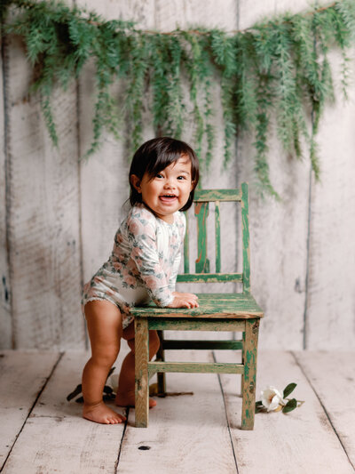 Enfant en studio, debout à côté d'une chaise, fond bois clair blanchi