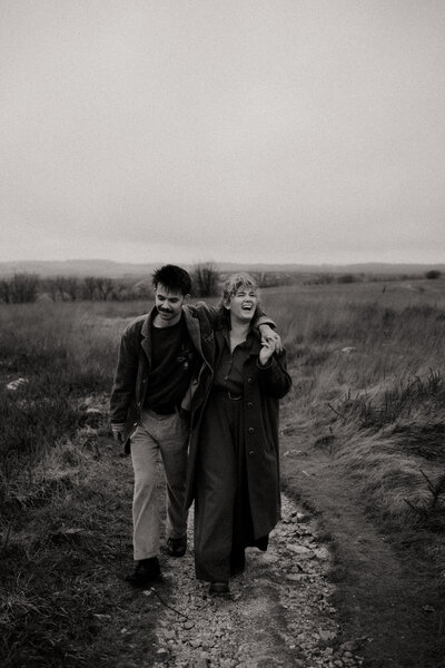 Léa et Nolan, photographe et vidéaste en Bretagne, marchant vers la caméra, bras dessus bras dessous, dans un décor de plaine.