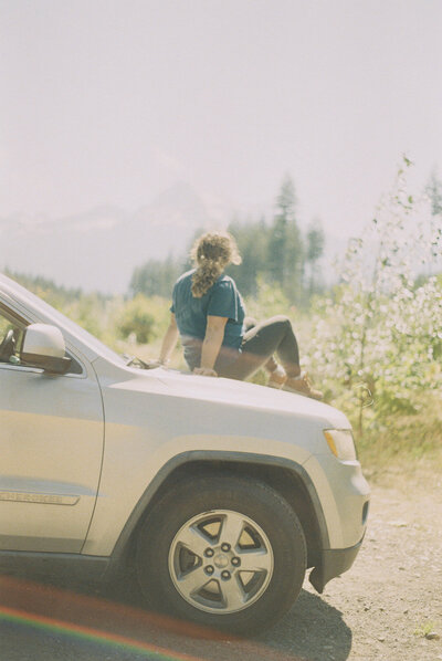 Sara Dobbins sits on hood of suv looking out at field