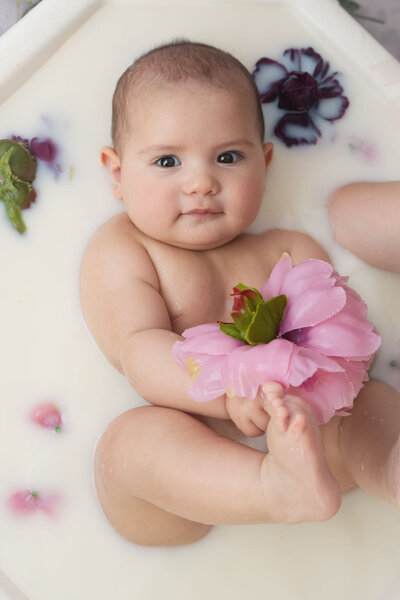 mum seated holding happy toddler smiling, with flowers in foreground