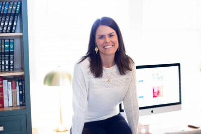 Jess sitting on desk in her coaching office next to computer