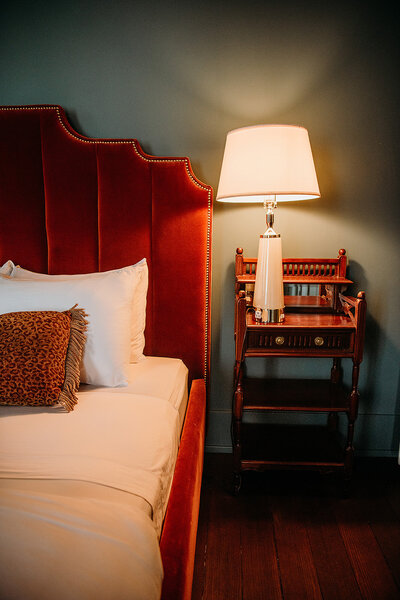 Deep Red velvet headboard, white crisp linens, dark blue wall with bedside lamp on