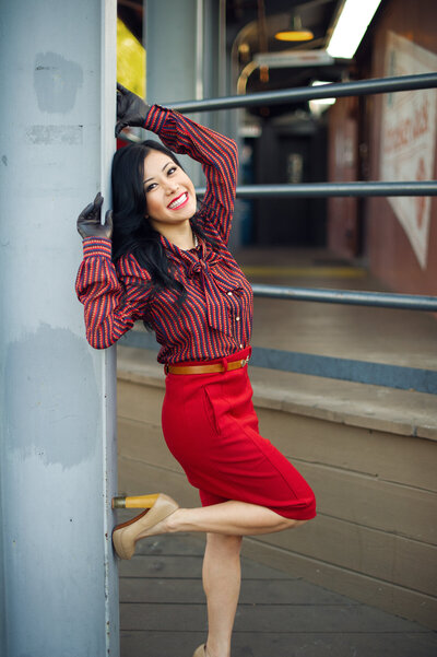 An Asian travel agent wearing a vintage silk shirt and red skirt for a personal branding photoshoot by a train station in San Juan Capistrano, CA.