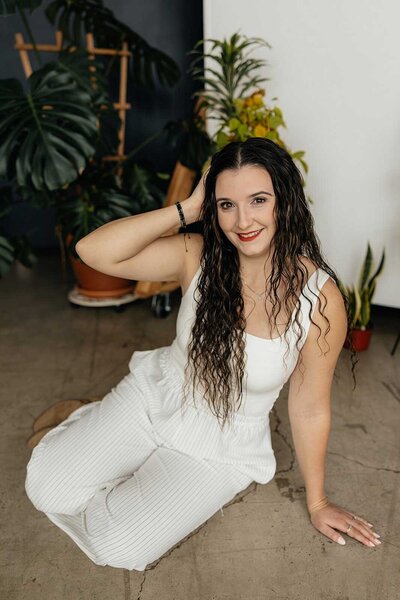Taysha smiling at the camera with her hand in her hair and plants behind her.