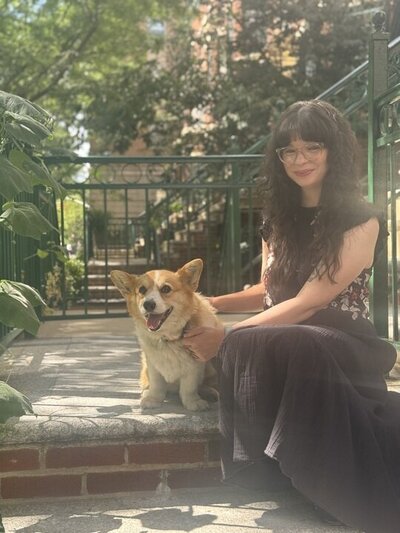 Team member sitting on outdoor steps with a small dog, surrounded by greenery