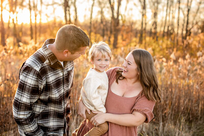 Mom and dad hugging on their toddler son while everyone is smiling.