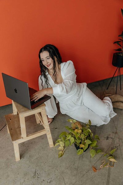 Taysha working on a laptop laying on the ground surrounded by plants.