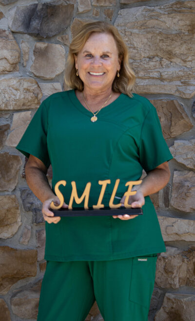 Mary Pat King posing for a headshot behind a rustic stone wall. 