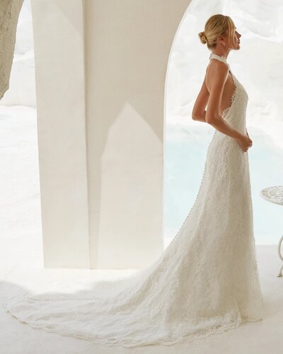 Bride in a halter lace gown with long train, standing by a white archway.