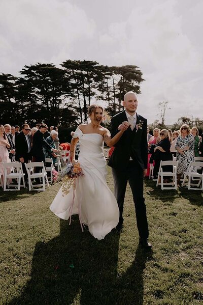 Bride and groom walking down the aisle after an outdoor wedding ceremony in Perth, surrounded by cheering guests.