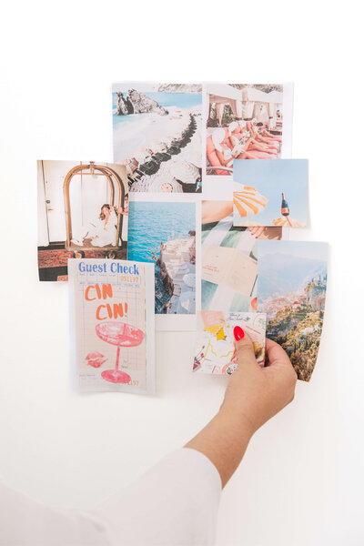Leith's hand placing images on moodboard, collaged on a red wall. Bright red nail polish