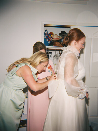 Flash film photo of bridesmaids adjusting the back of bride's dress