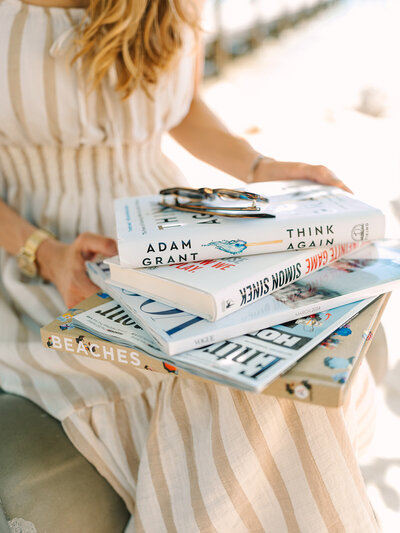 Stack of books in the lap of woman wearing tan and white striped dress