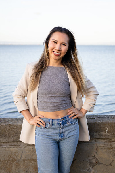 Modern portrait of Ellen Lai in jeans and blazer posing confidently near the ocean, captured by Ellobelle Photography Family Photographer