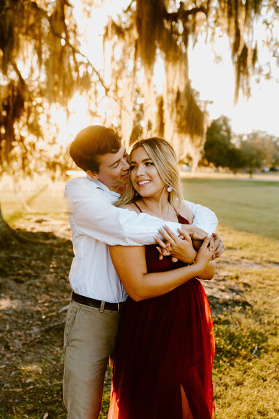 Couple hugging each other under mossy tree in Mandeville, LA