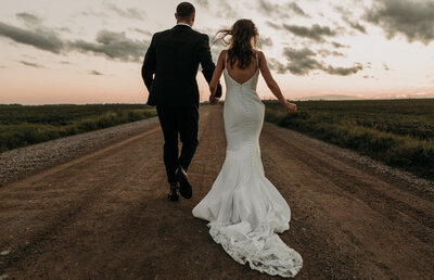 bride and groom running down gravel road