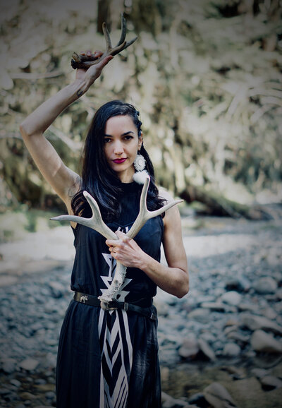 Founder of Alchemy Queen holding deer antlers in front of her heart. 