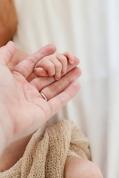 Close-up of tiny baby hands holding mothers hand, capturing delicate newborn details in soft natural light. Lifestyle photography by Sophie Louise.
