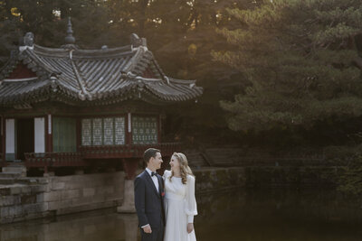 bride in a white dress and a groom in a navy blue tux pose at Changdeokgung Palace in Seoul