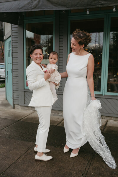 Two women stand with their baby for wedding photos prior to their intimate ceremony at Fairweather Restaurant in Portland, Oregon.