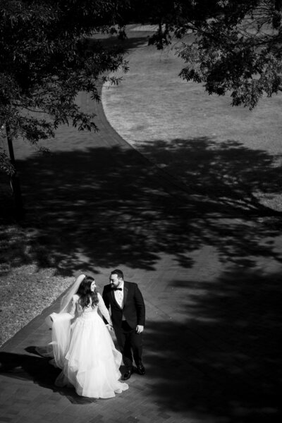 Black and white photo of bride and groom holding hands walking.