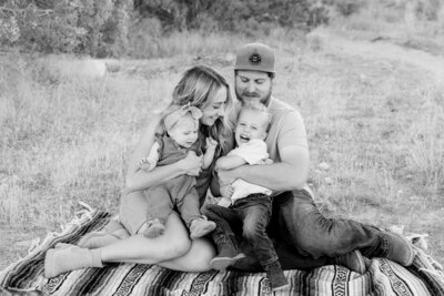 Cute family shares a fun moment while having a tickle fight on a blanket outdoors.
