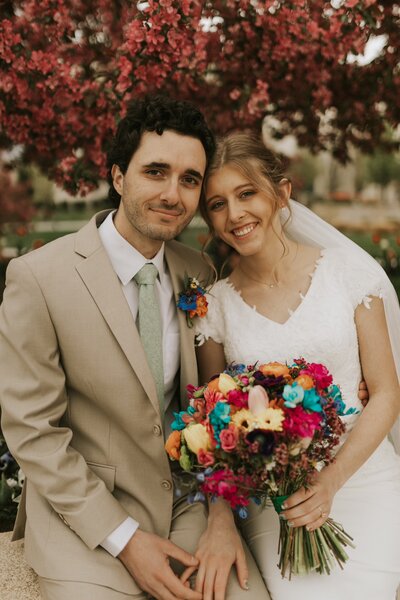 groom sitting next to bride holding bright and beautiful bouquet made by Buds Blooms and Blossoms