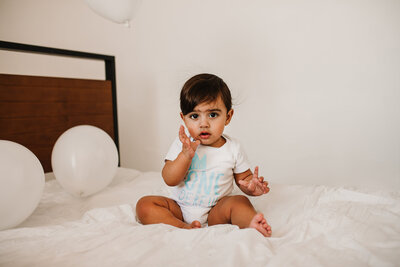 baby sitting on bed with white balloons