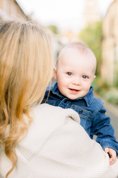 Adorable baby peeking over his blonde mothers shoulder.