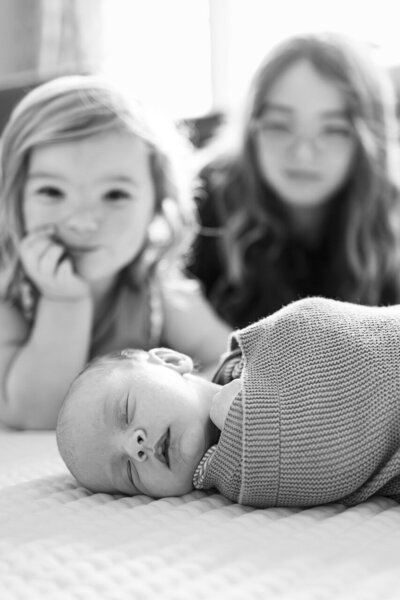 Beautiful lifestyle newborn photography in Tifton, Georgia: Focus on sleeping newborn baby in the foreground with big sister's looking on