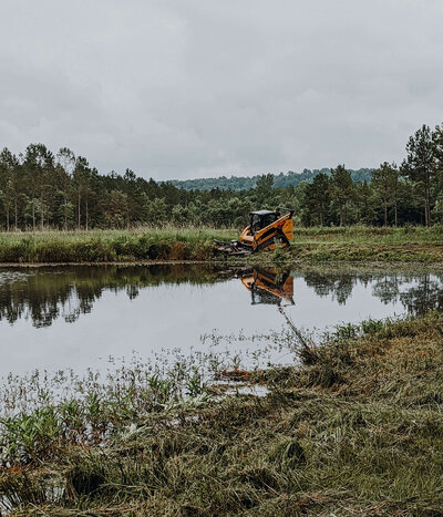excavator-cleaning-up-brush-around-edge-of-pond-on-a-cloudy-day